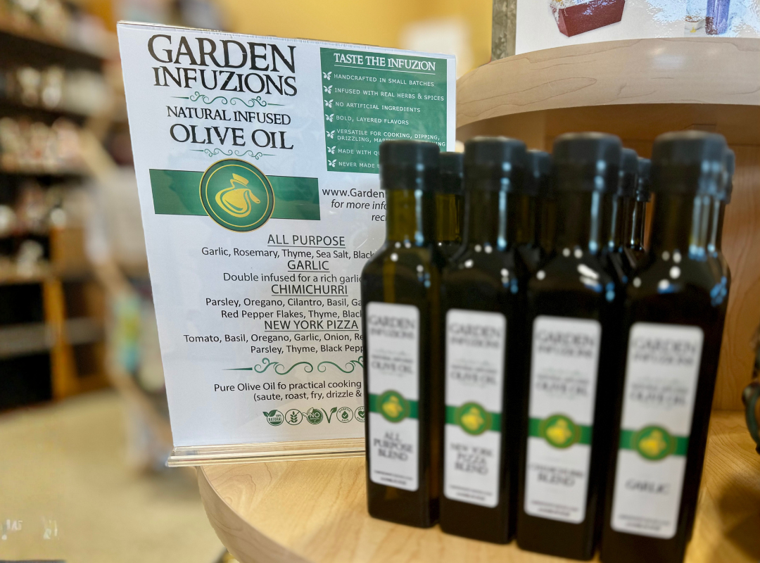 Small bottles of Garden Infusions olive oil displayed beside a product sign on a wooden shelf.