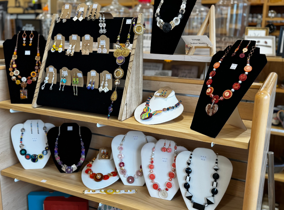 Display of colorful handmade jewelry on black and white necklace stands at a market stall