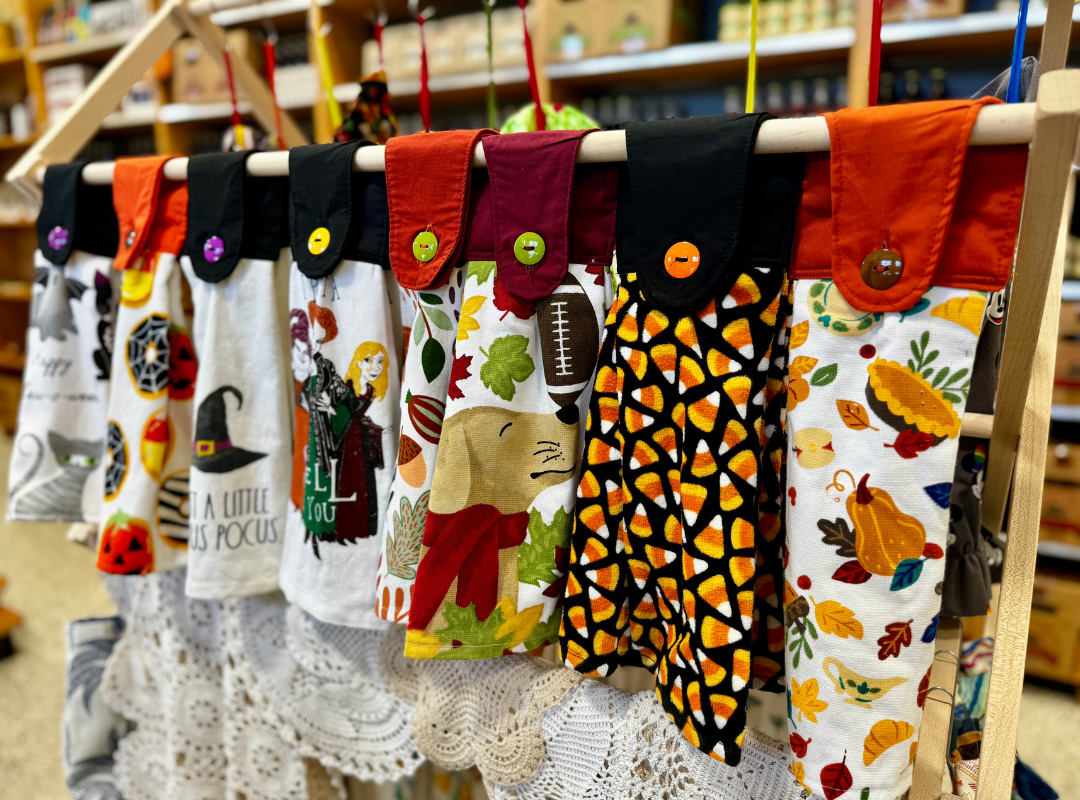 Colorful hanging kitchen towels with fall and Halloween patterns displayed on a store rack