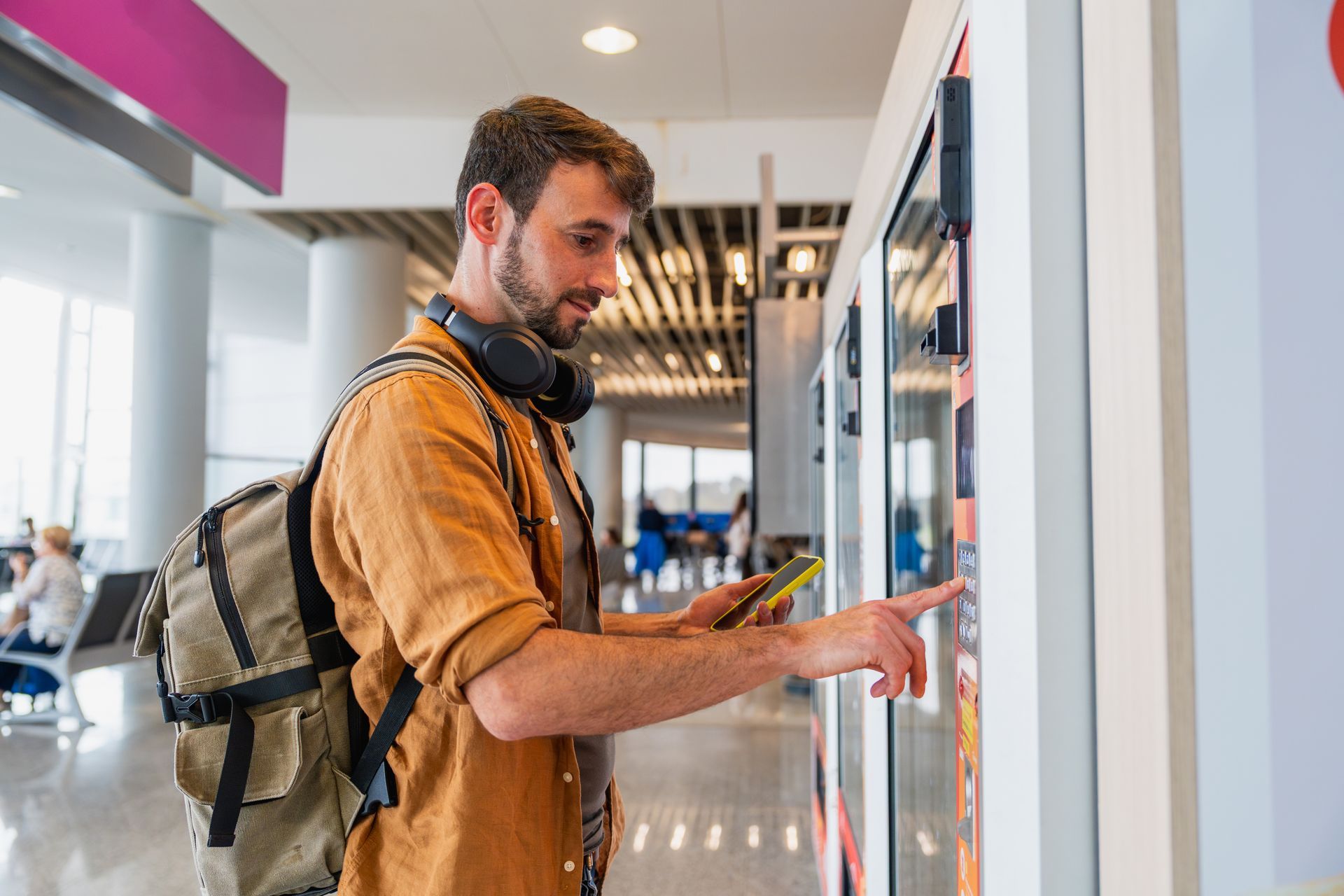Traveler with backpack using a vending machine in a modern transit terminal.