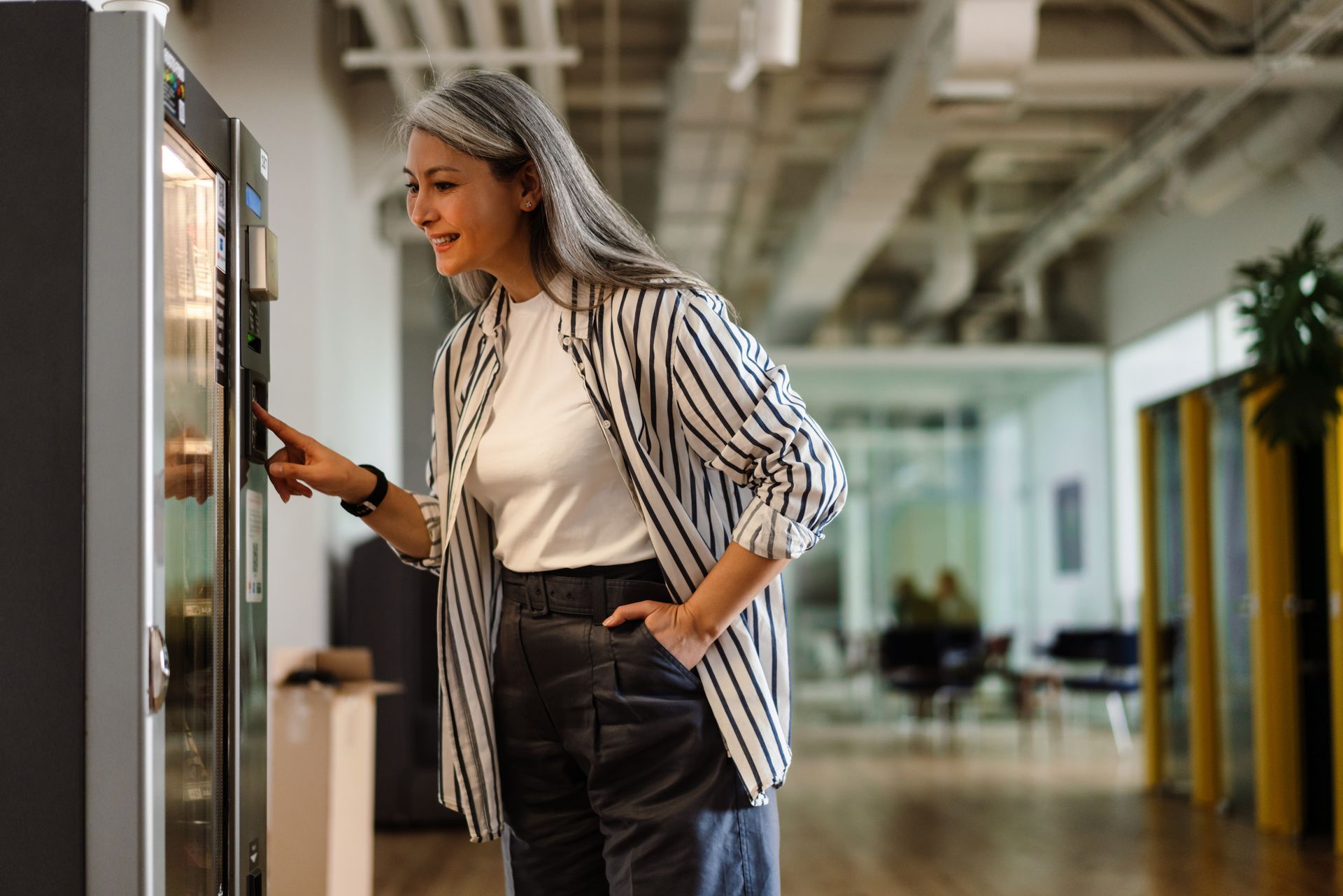 a woman in casual business attire selecting an item from a vending machine in a modern office setting. a woman in casual business attire selecting an item from a vending machine in a modern office setting.