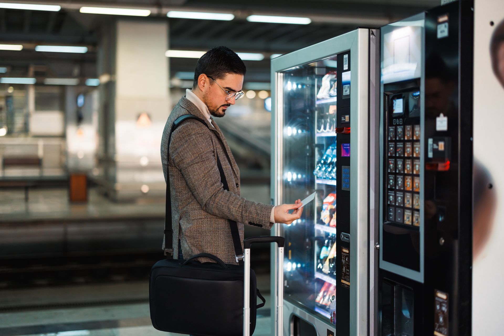 A businessman with glasses grabs a healthy snack from a sleek fresh market vending machine.