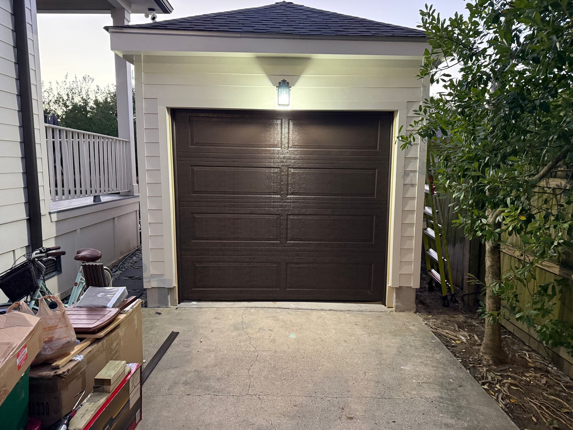 Brown garage door with a light above, set in a white-trimmed building, on a concrete driveway.