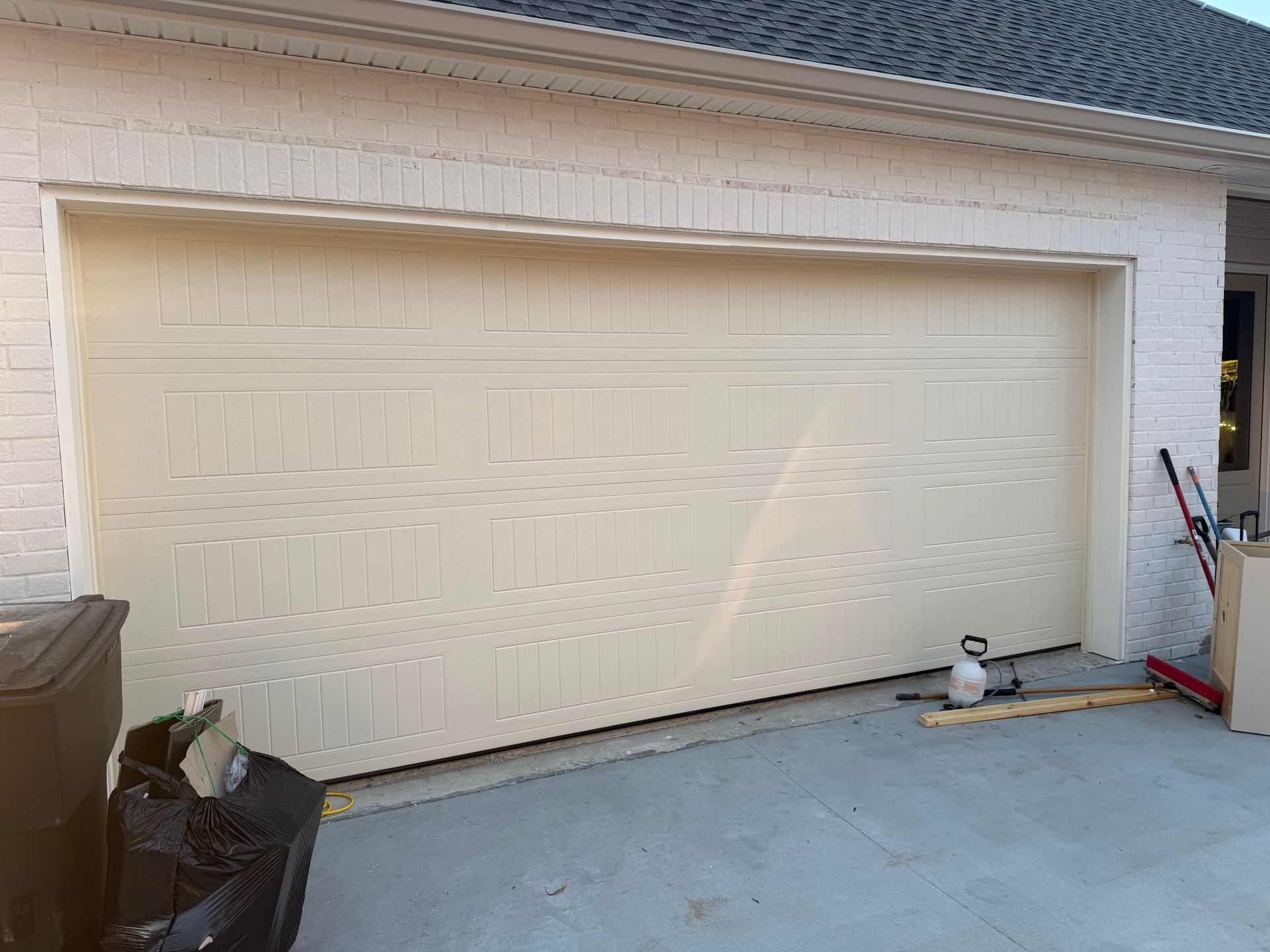 Beige garage door on a brick building; partially open on a concrete driveway.