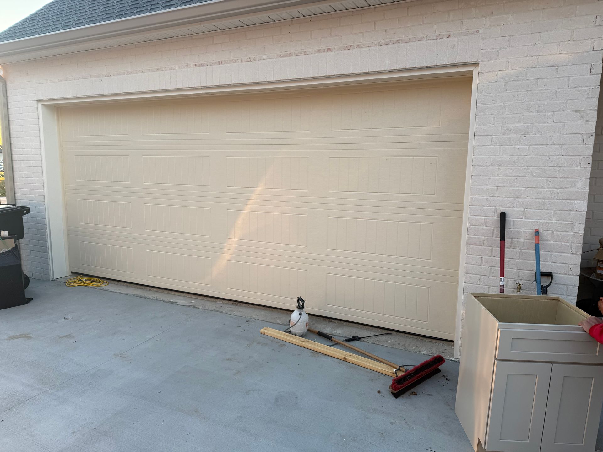 Beige garage door on a light-colored brick building. Construction materials are scattered in front.