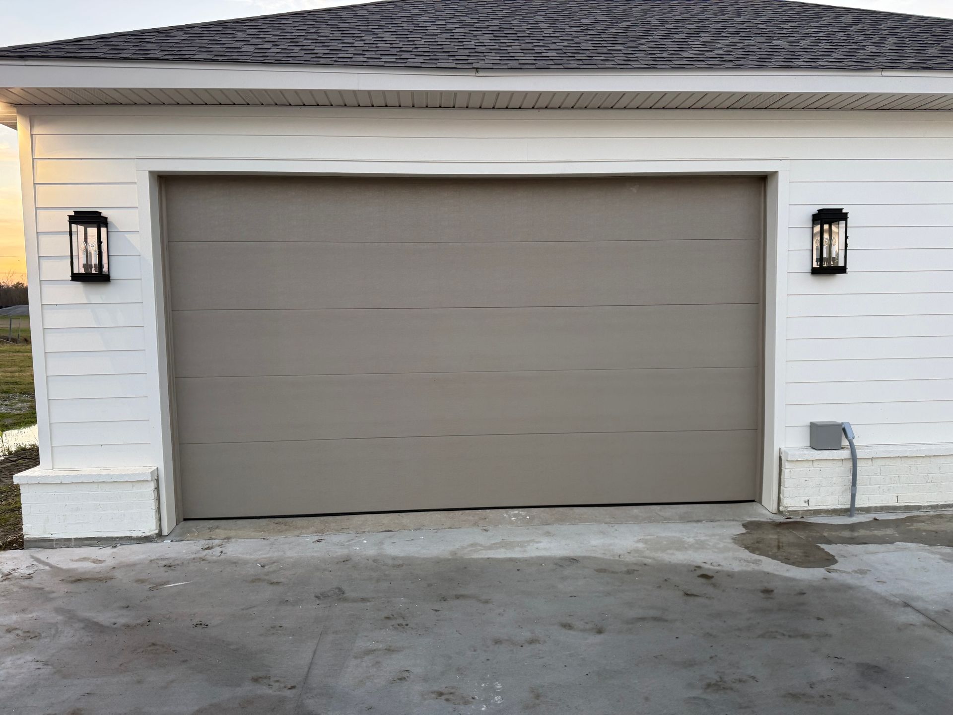 Tan garage door with two black lights, set in a white exterior.