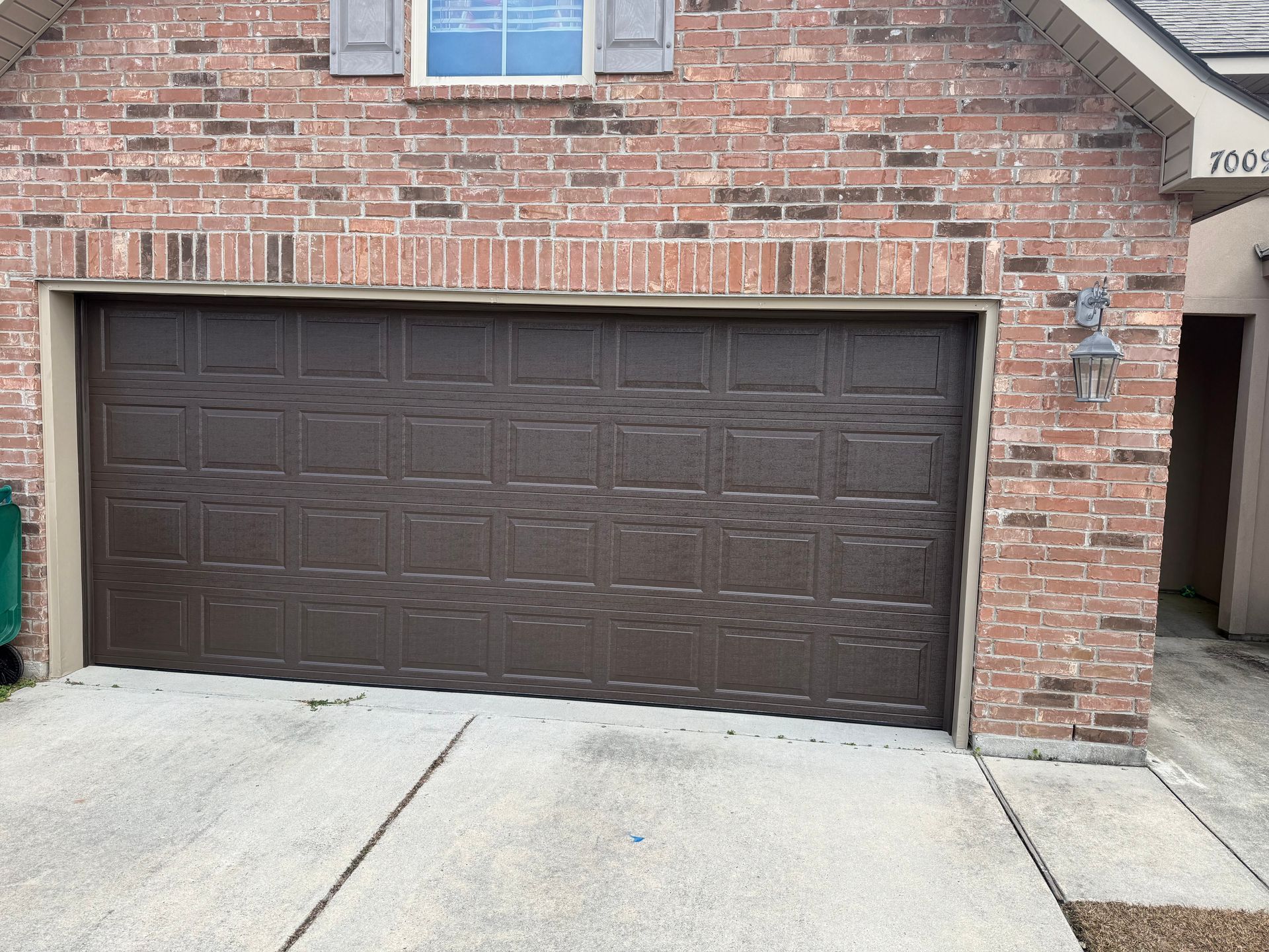 Brown garage door on a brick house. Concrete driveway.