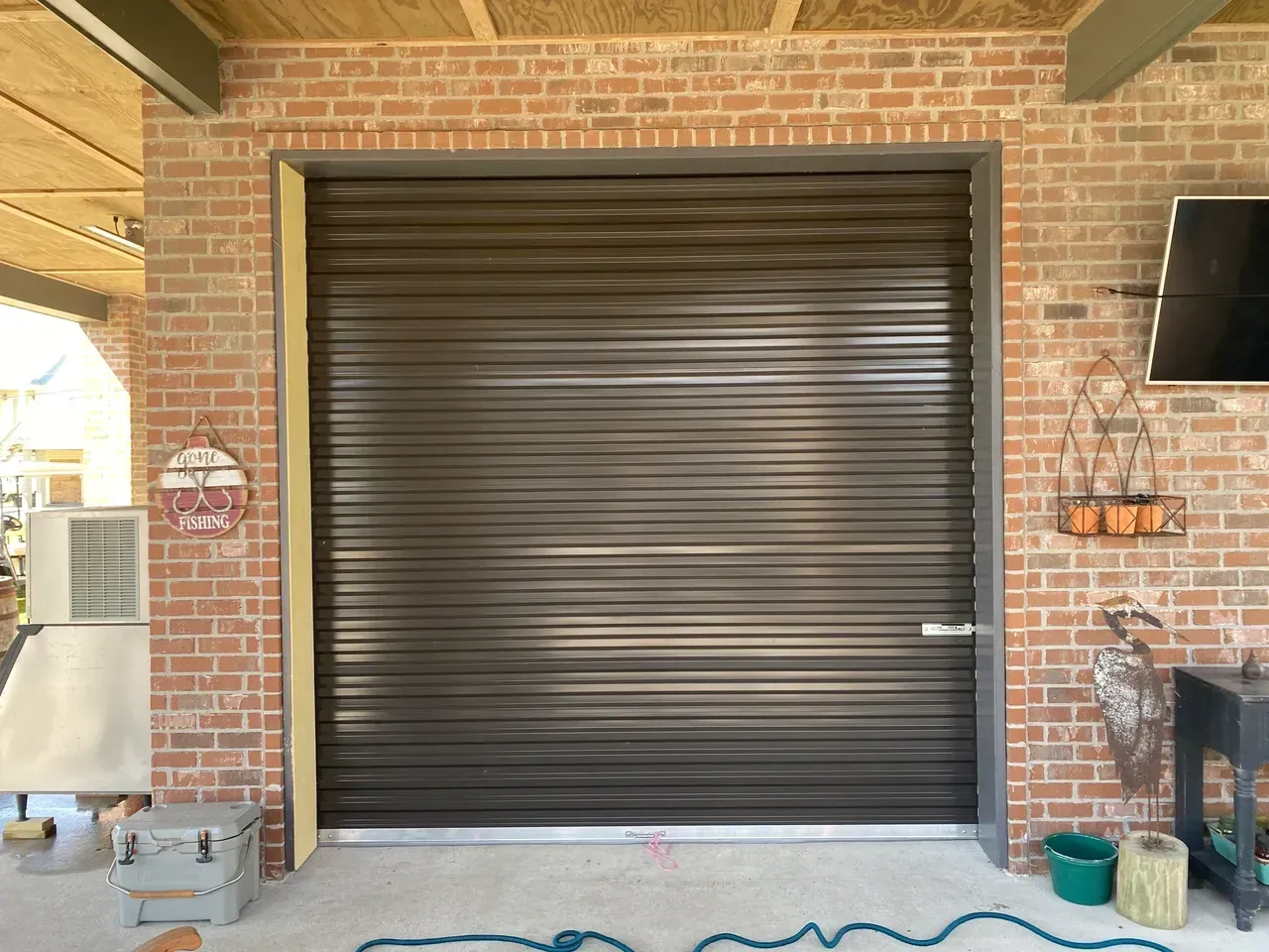 Brown metal roll-up garage door on brick building with concrete floor; outdoor setting.
