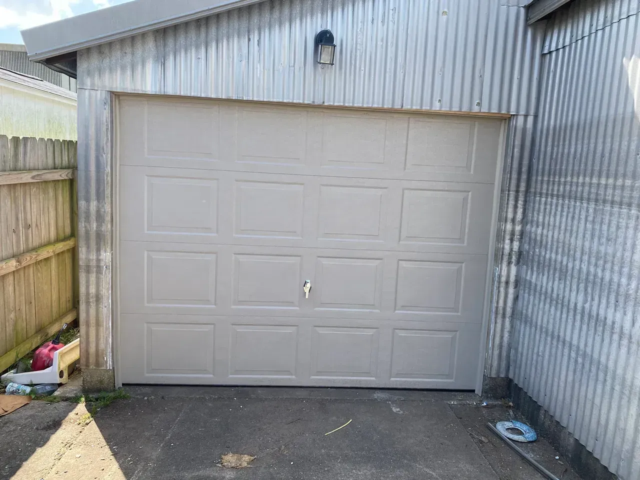Tan garage door with square panels, mounted on corrugated metal building.