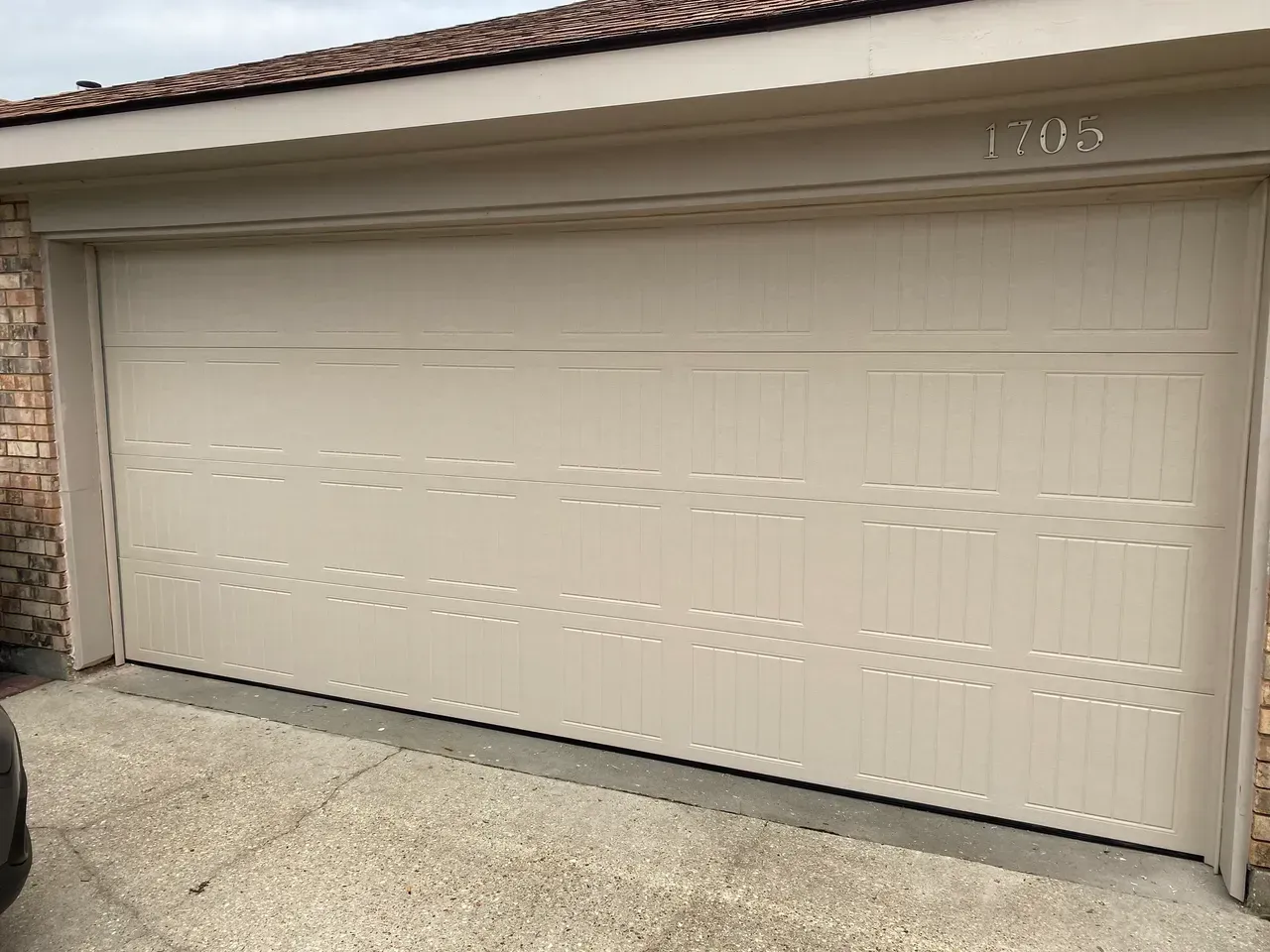 Beige garage door with vertical lines, address number 1202 above, concrete driveway.