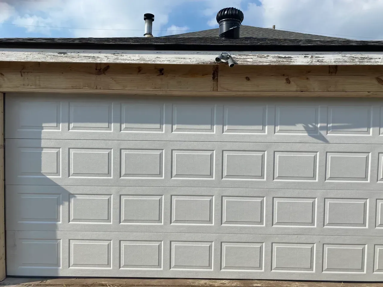 White garage door with rectangular panel design, beneath weathered roofline.