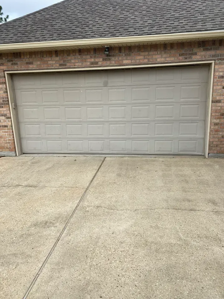Tan garage door on a concrete driveway, set in a brick building.