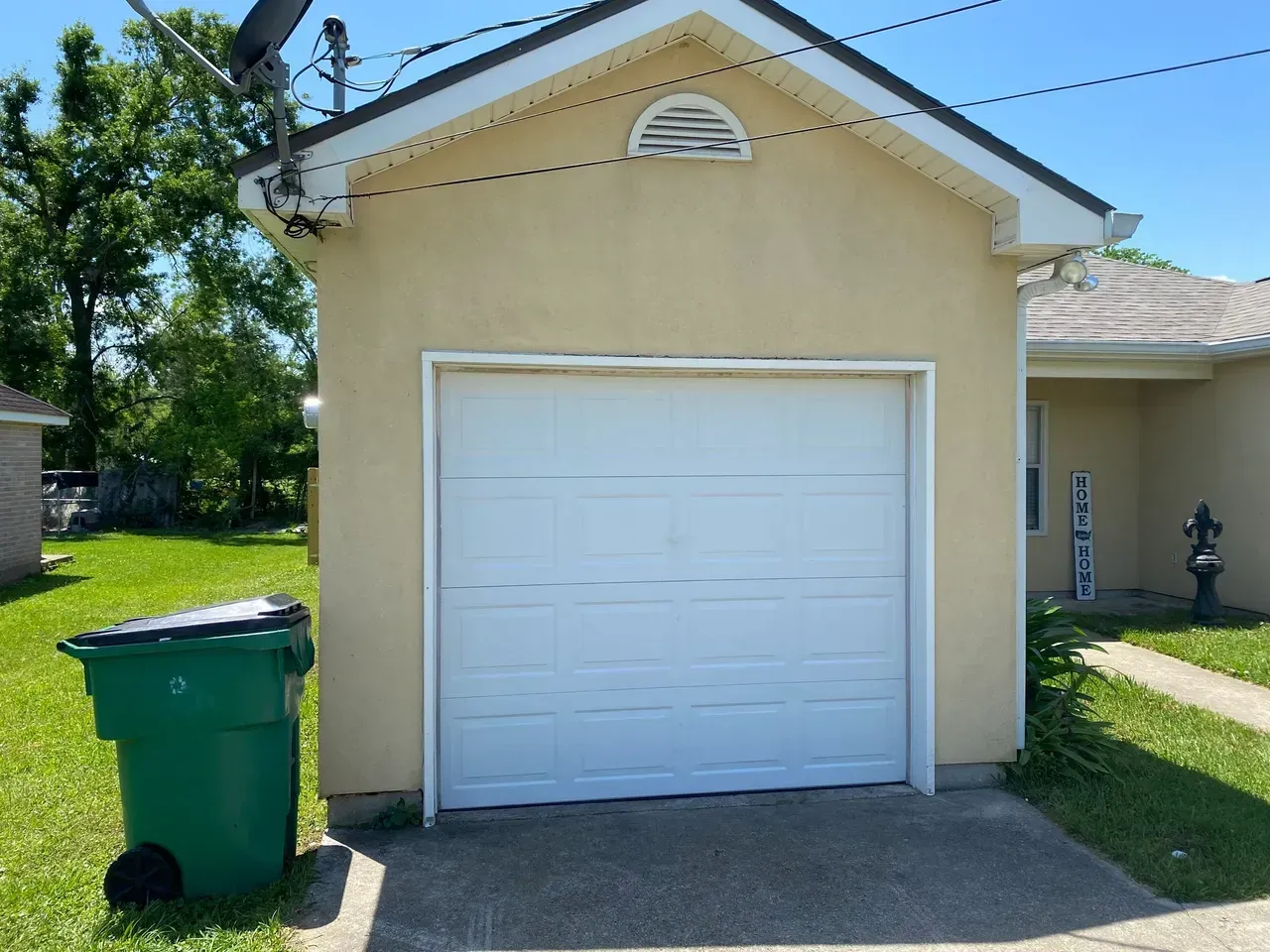 A detached garage with a white door, yellow walls, and a green trash can.