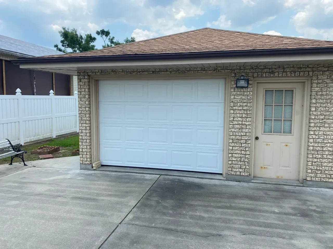White garage door, tan brick building with small door, concrete driveway.