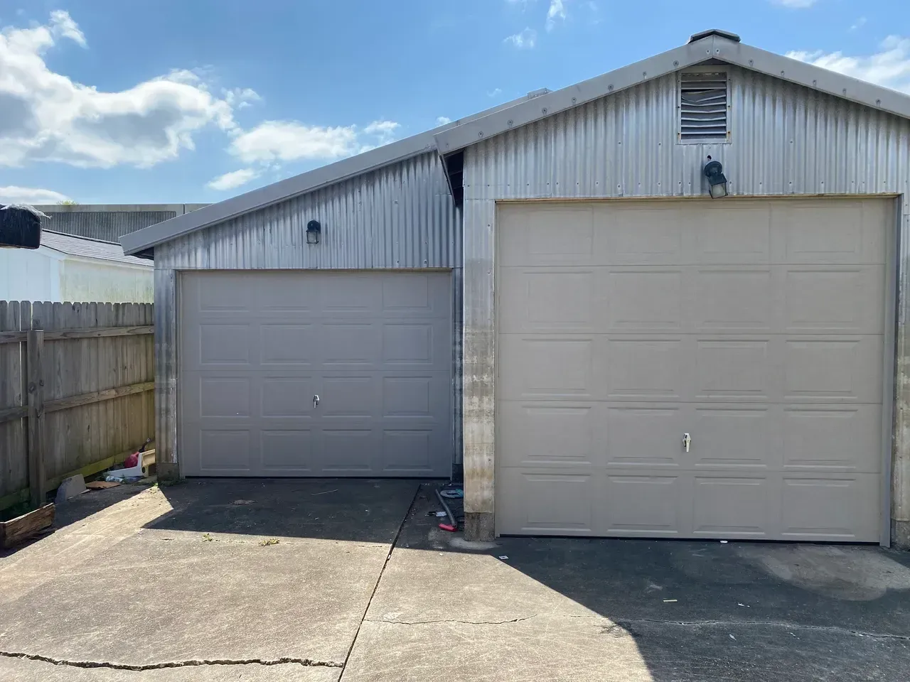 Two gray garage doors in front of a metal building. Concrete driveway in front.