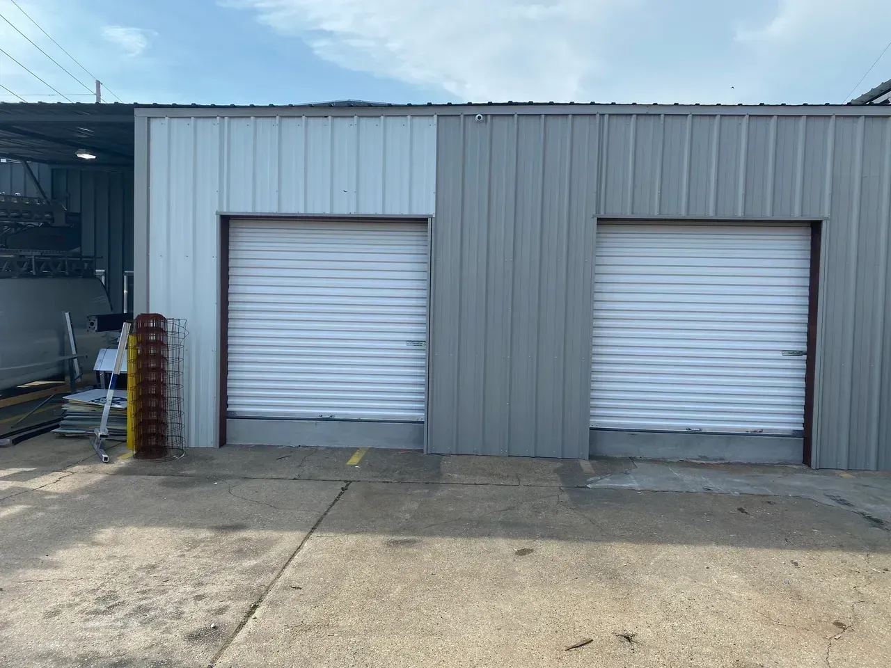 Exterior view of two garage doors in a light and medium gray metal building, on a concrete surface.
