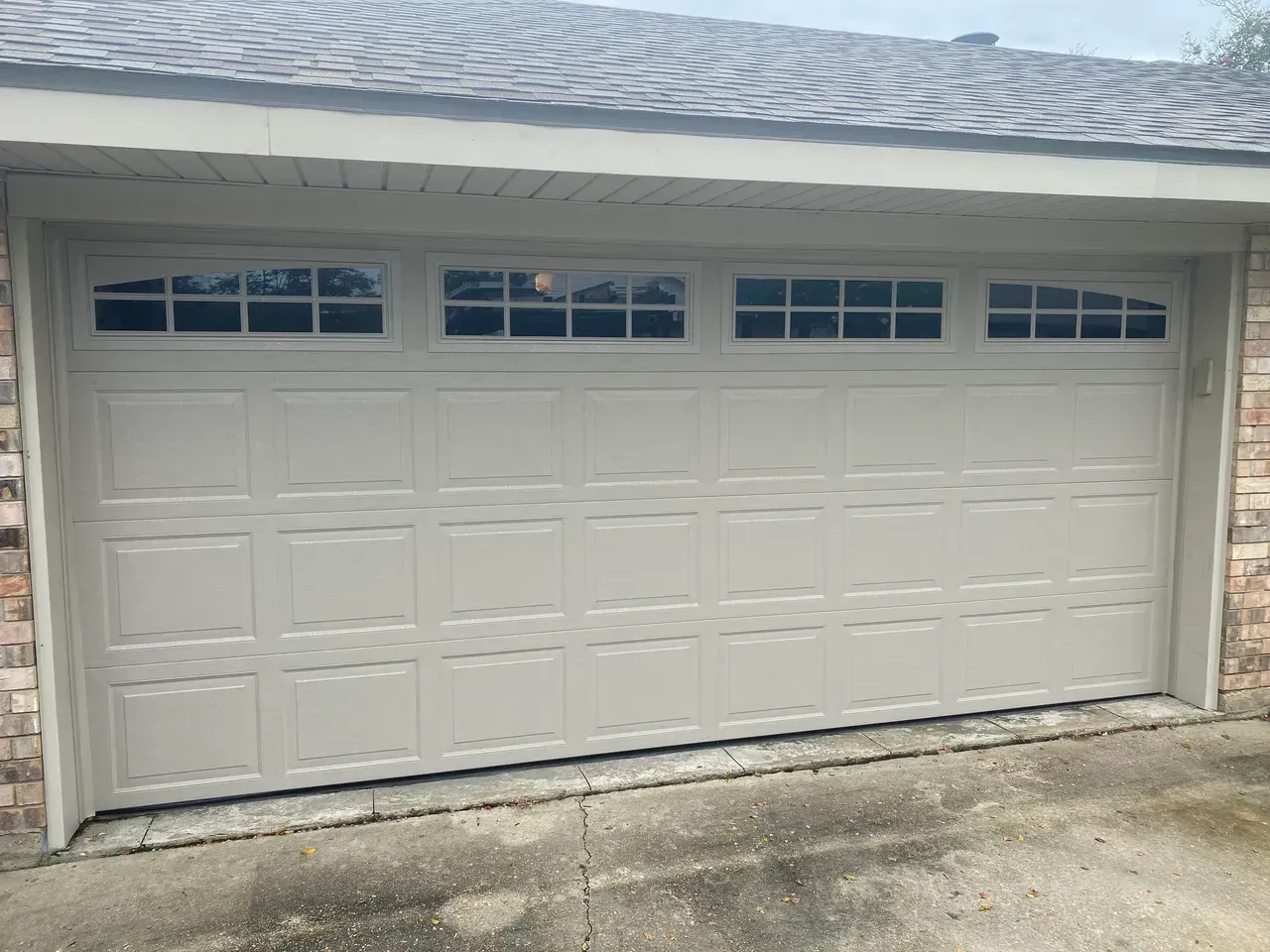 Tan garage door with windows above; brick and siding exterior.