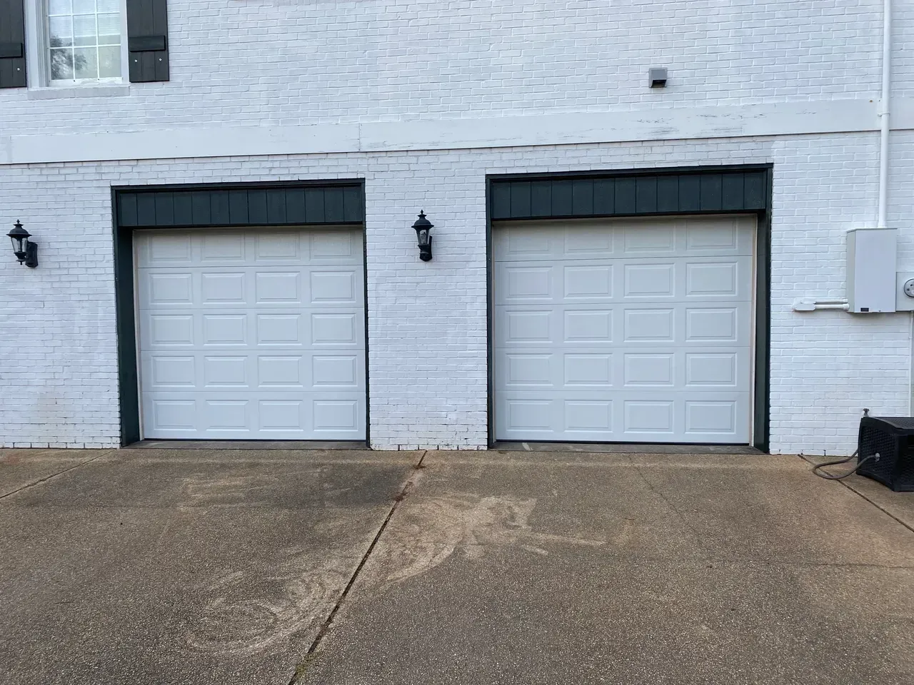 Two white garage doors on a white brick building. Gray concrete driveway. Black trim.