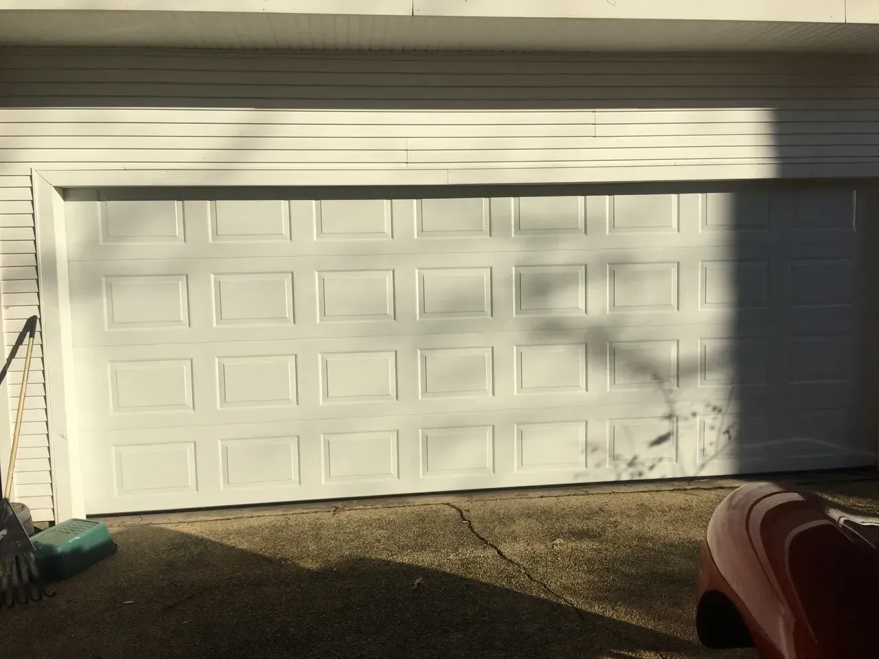 White garage door with grid pattern, partially shadowed, set against white siding.