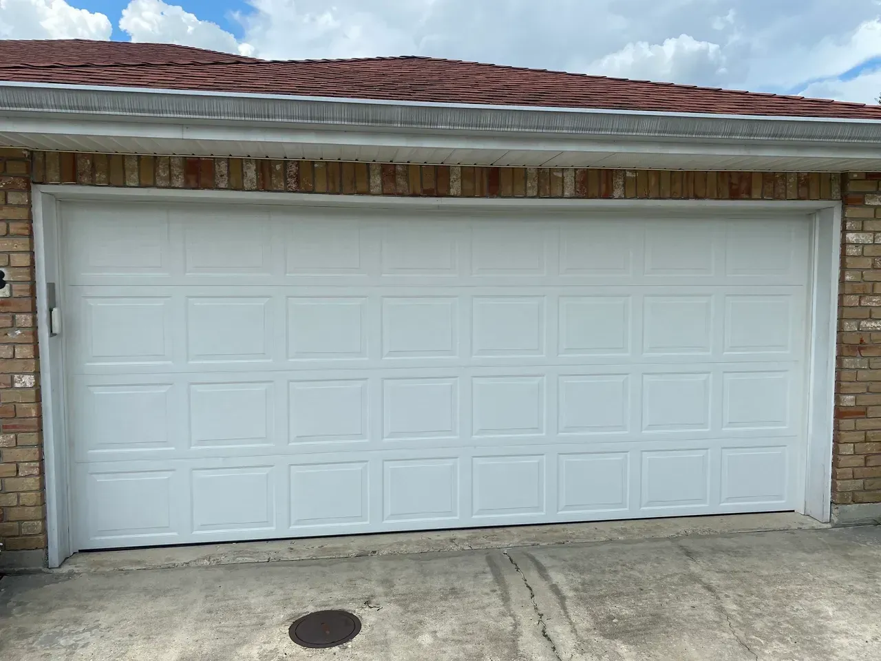 White garage door in a brick building under a red roof.