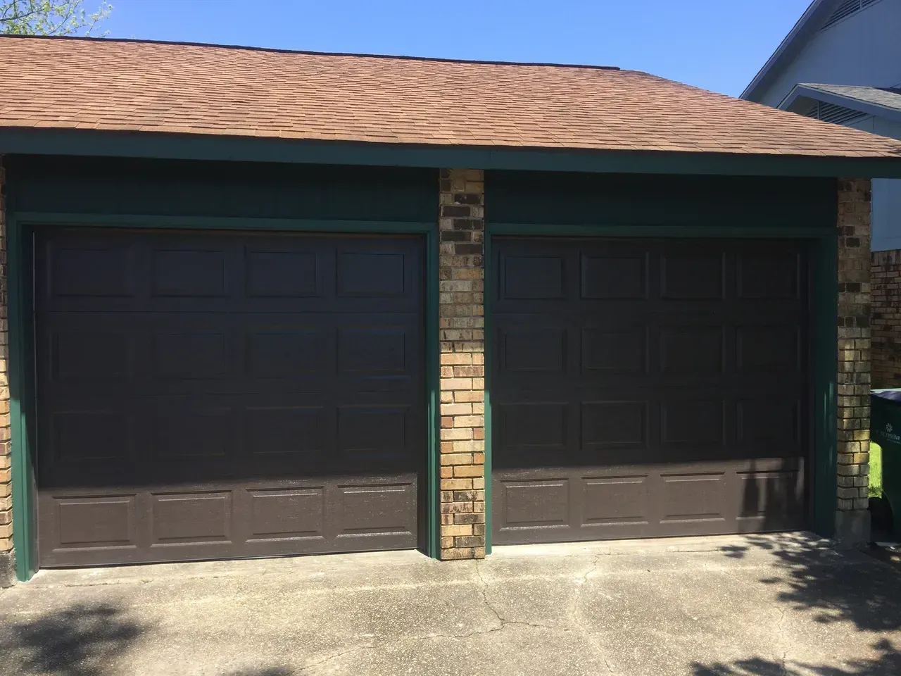 Brown garage doors under a brown roof, flanked by brick and green trim.