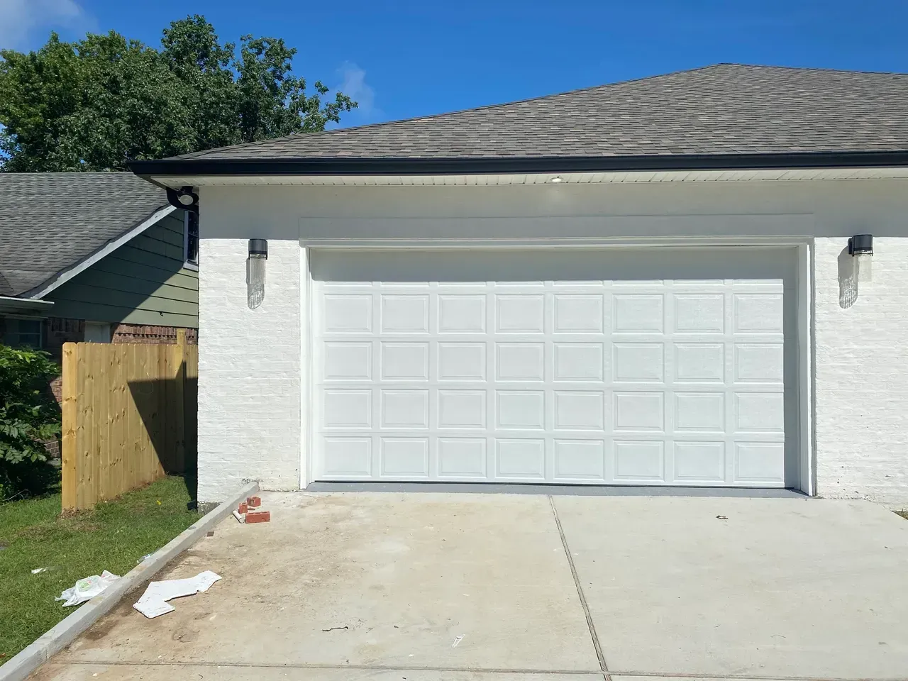 White garage door on a white brick building under a gray roof on a sunny day.