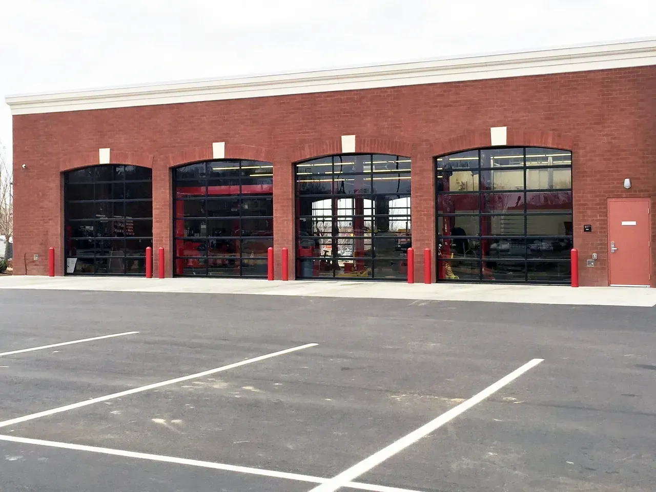 Fire station with four garage doors; red brick exterior, parked vehicles visible inside, empty parking lot.