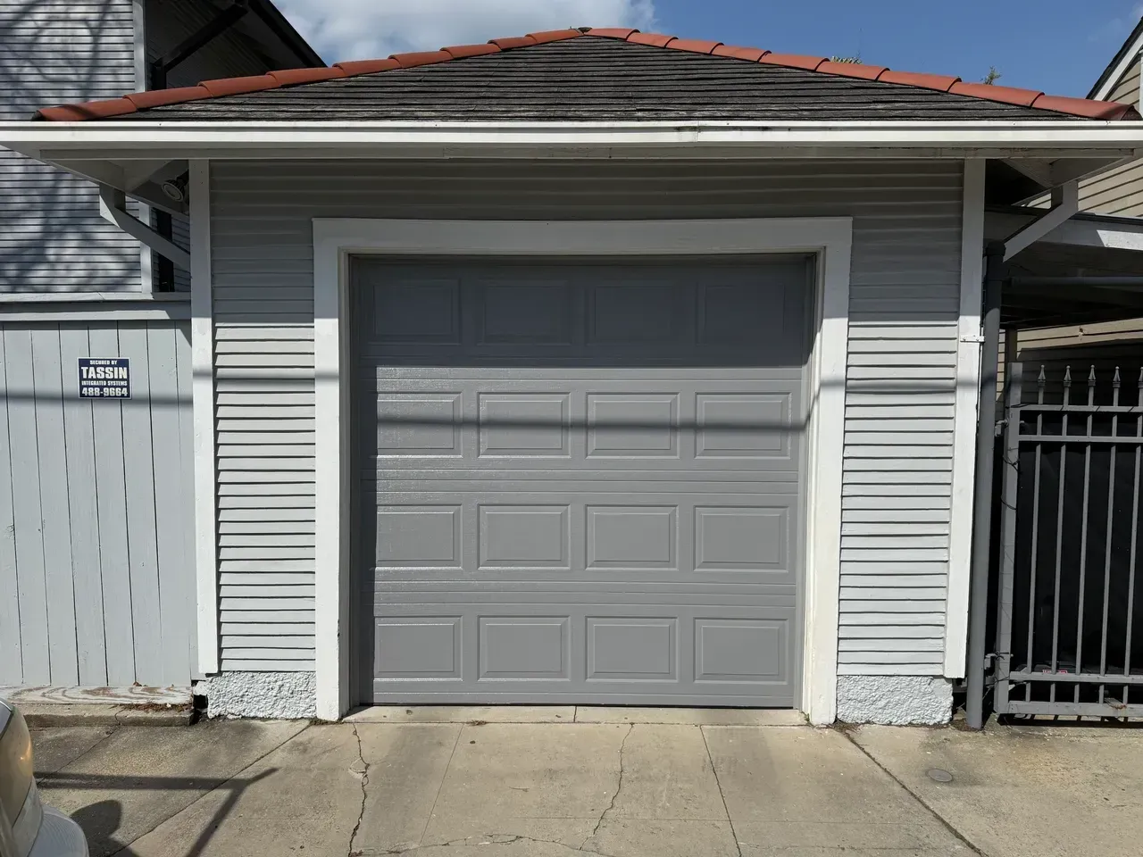 Gray garage with a closed gray door, surrounded by light gray siding and a red tile roof.