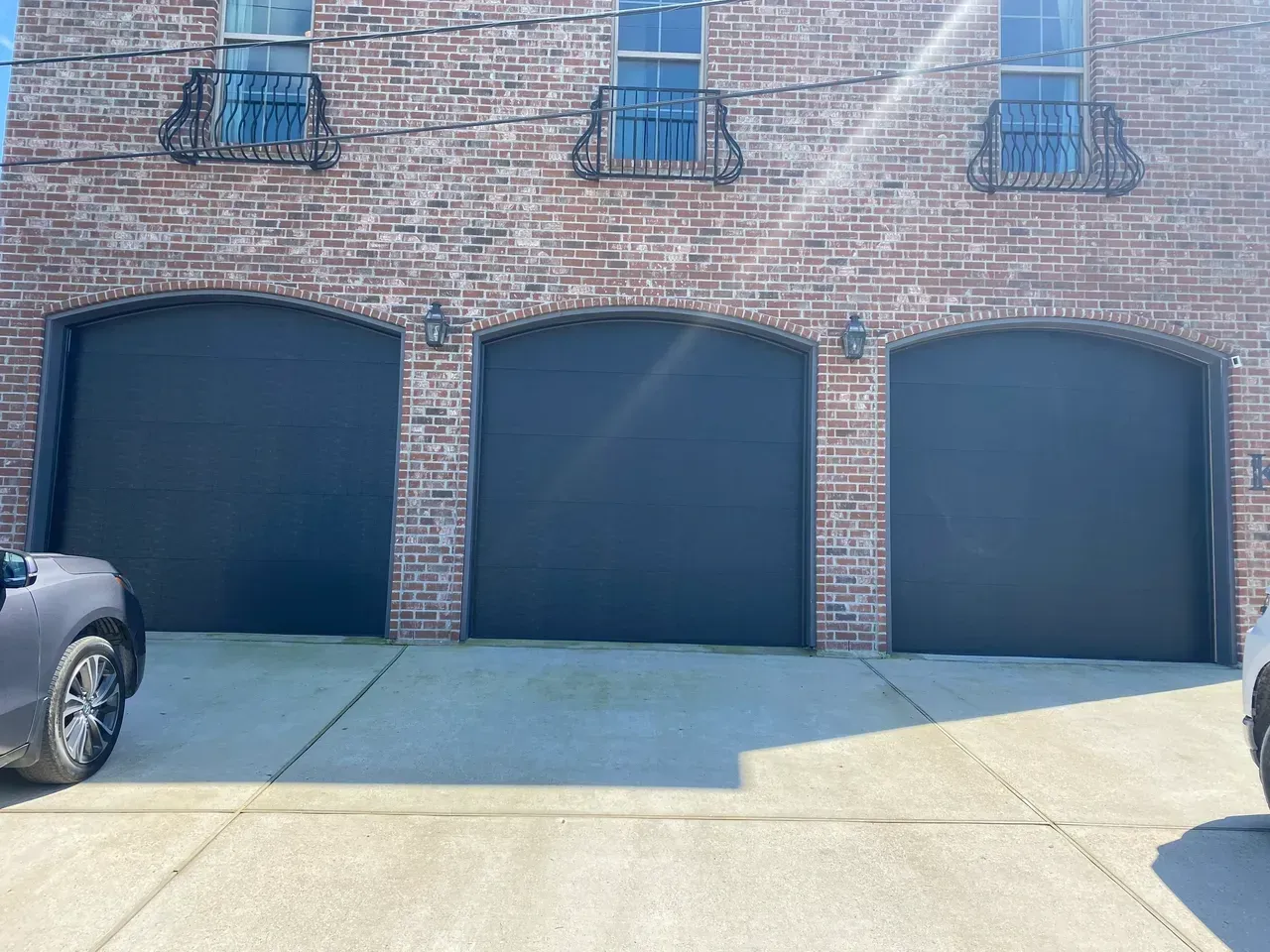 Three black arched garage doors on a brick building with decorative ironwork and windows above.