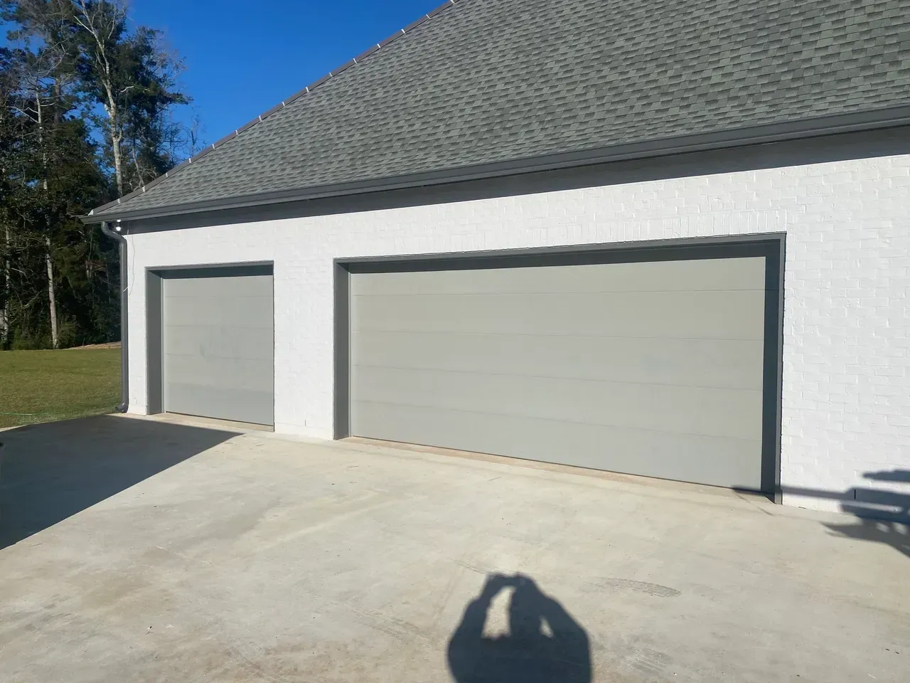 Two-car garage with gray doors, white walls, and a concrete driveway under a blue sky.