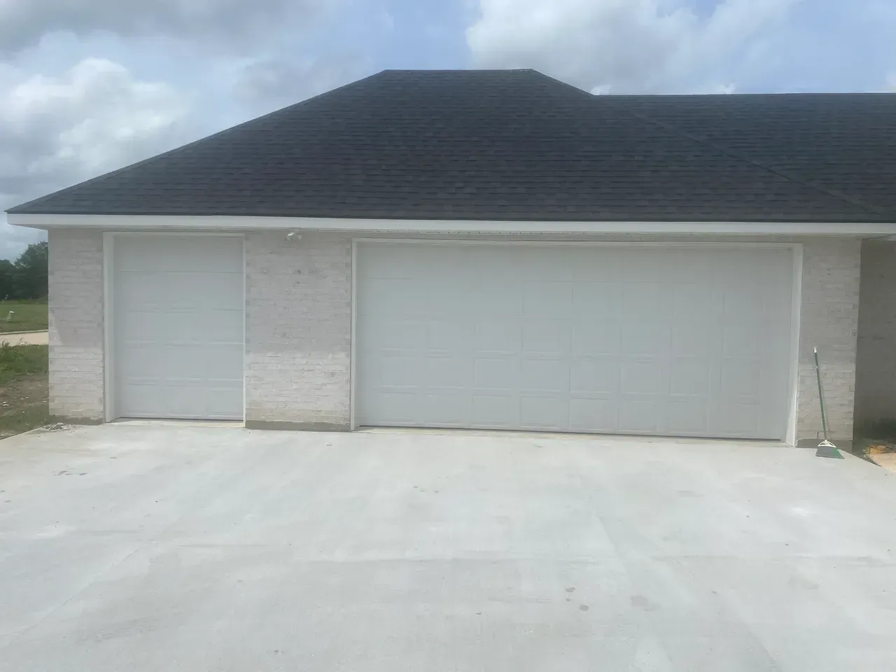 Two white garage doors on a light-colored brick building with a dark roof.