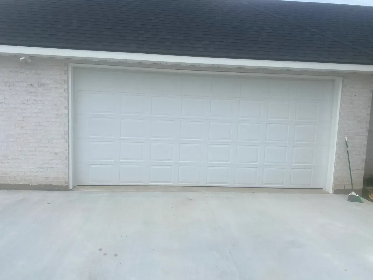 White garage door on a concrete driveway, flanked by light brick walls, set against a dark roof.