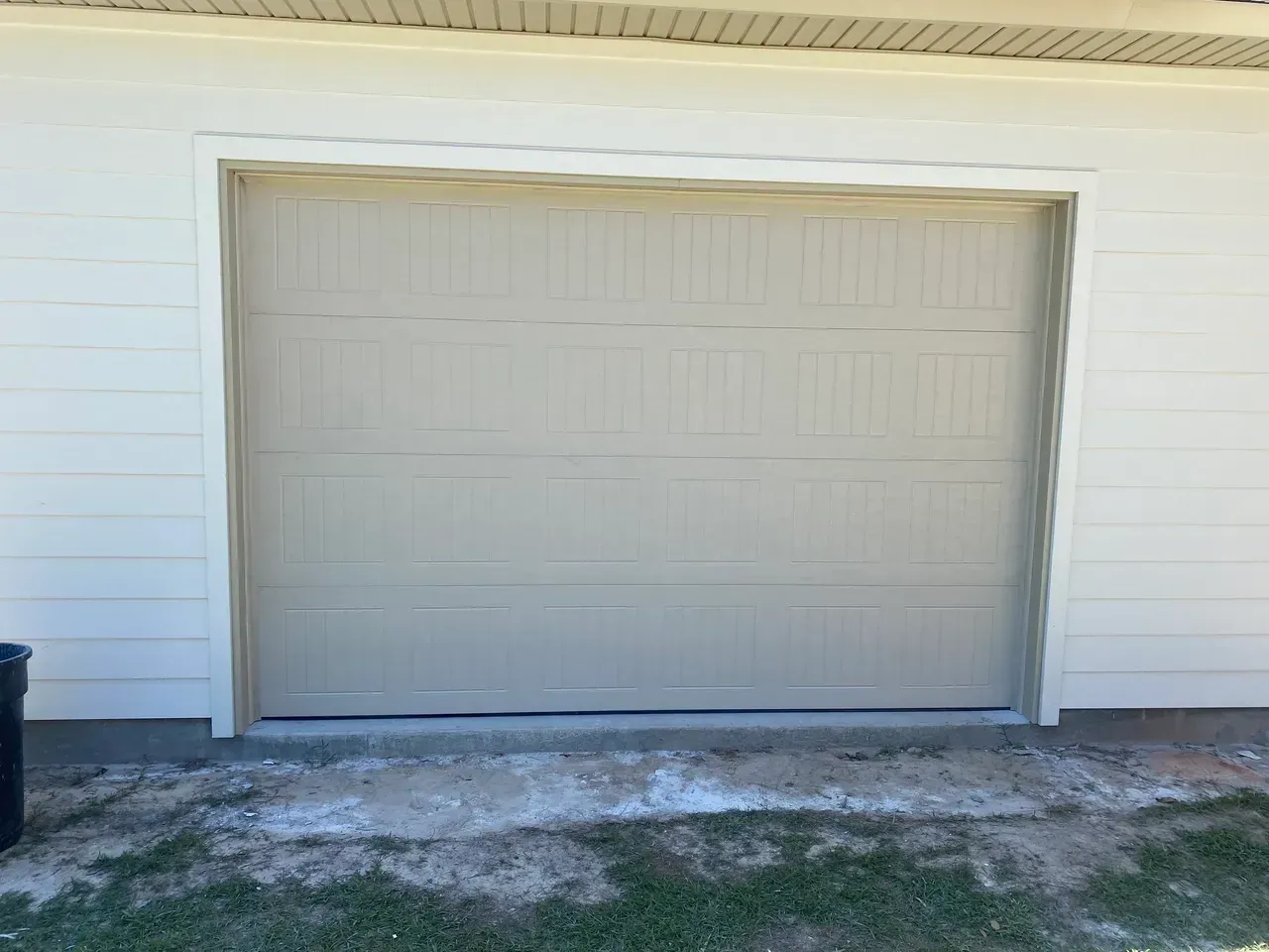 Tan garage door on a beige house, with white trim and a concrete base.