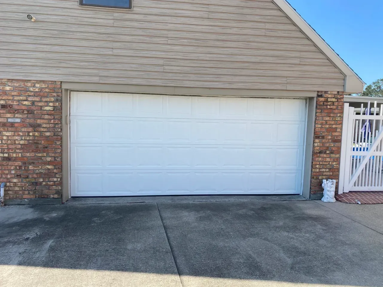 White garage door on a brick and siding building, in front of a concrete driveway.