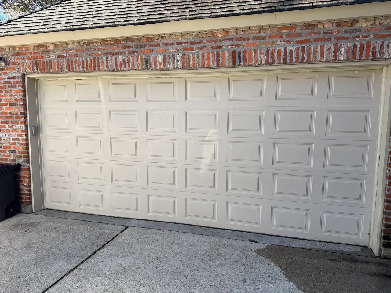Beige garage door with square panels, set in brick building.