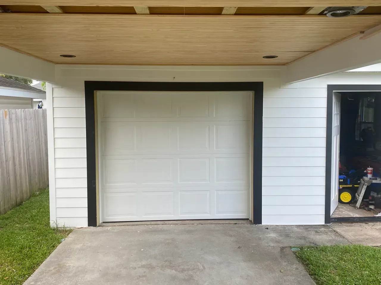 White garage door with black trim under a wooden ceiling. Concrete driveway.