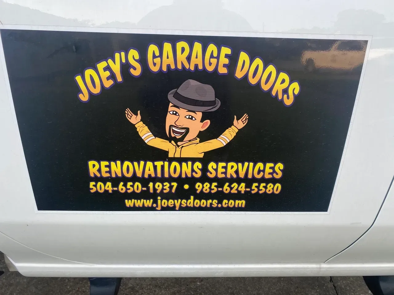 Joey's Garage Doors sign on a vehicle with logo of cartoon man with arms up, contact info, and website.