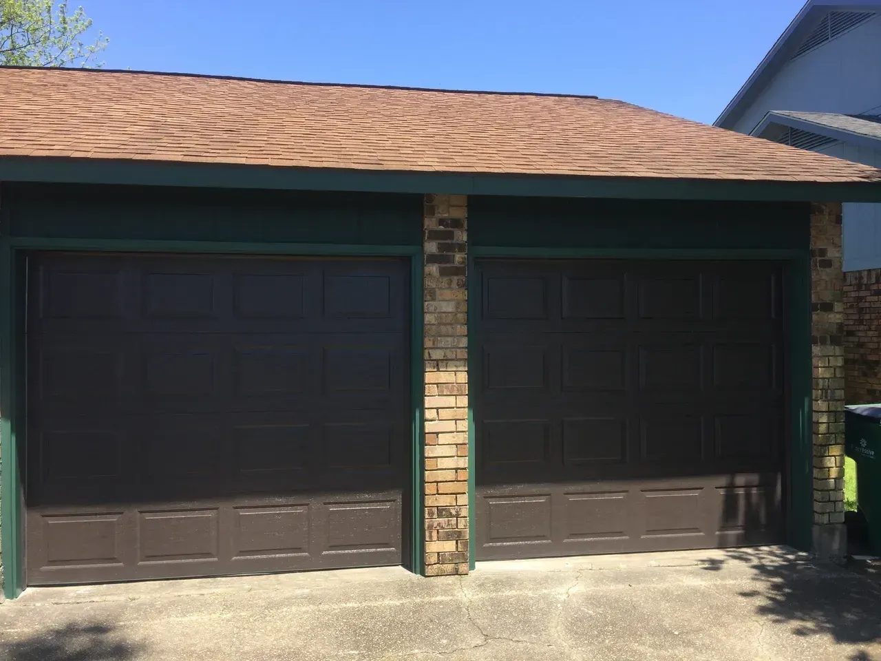 Brown garage doors with a brick column and brown roof against a blue sky.