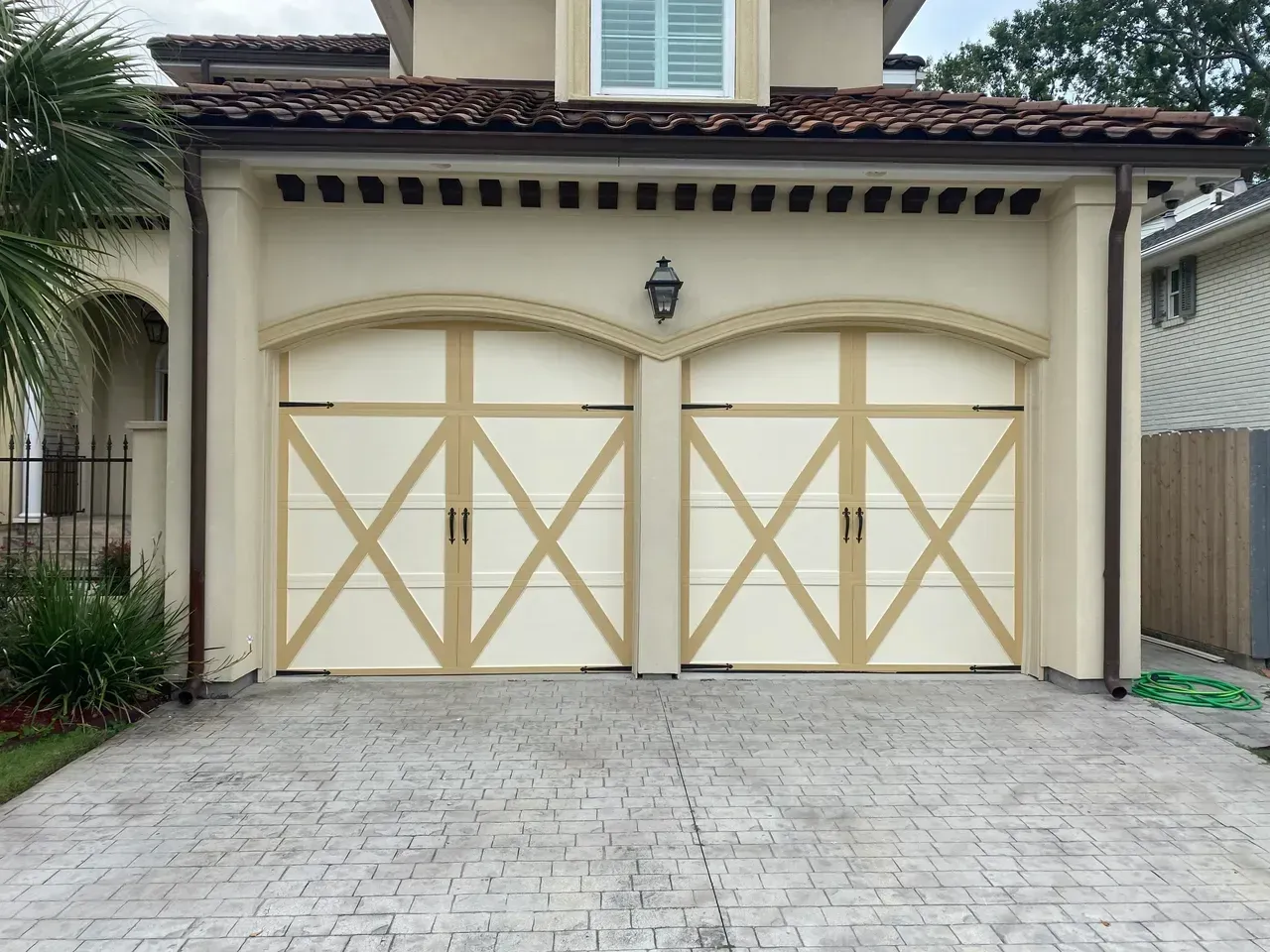 Two-car garage with cream-colored doors featuring beige crosses, set in a beige stucco building with a tiled roof.