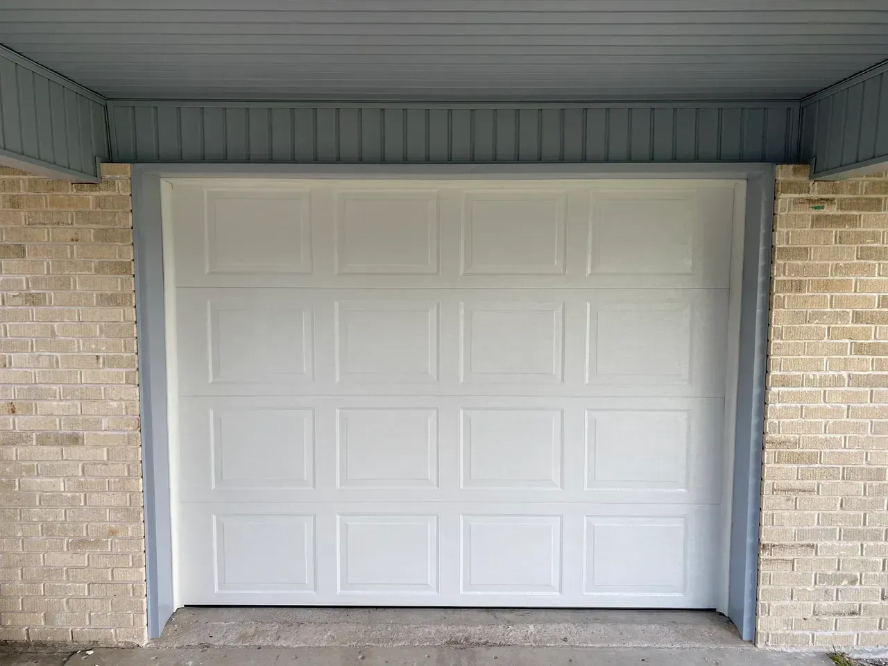 White garage door, light brick exterior with blue trim.