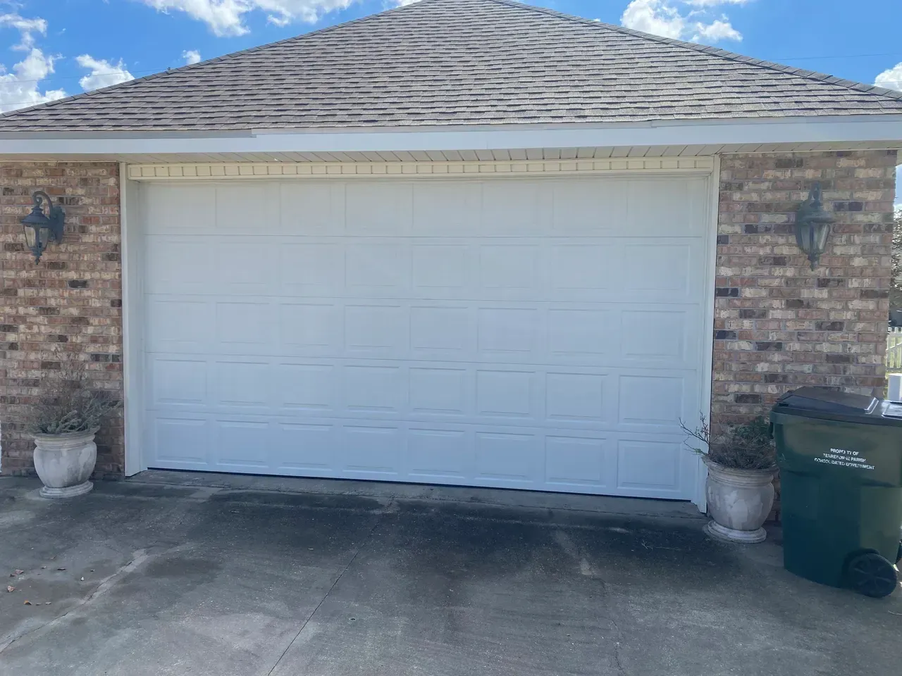 White garage door on brick building with potted plants and trash can.