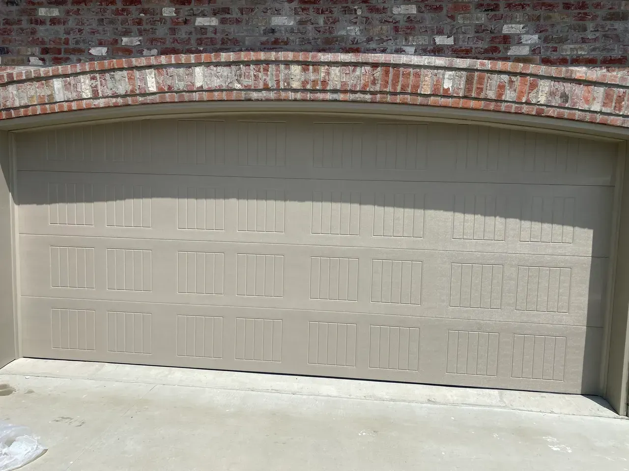 Tan garage door beneath a brick archway.