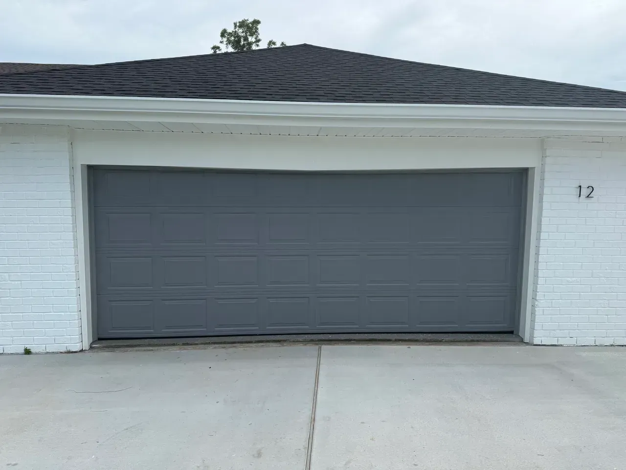 Gray garage door in a white brick building, number 12 above the door.
