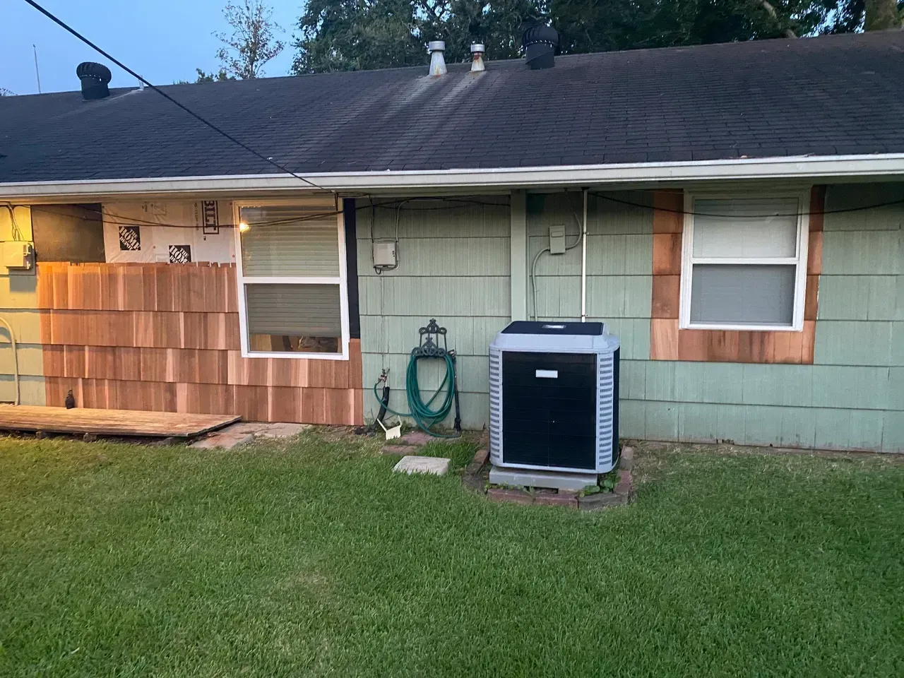 House exterior with cedar shake siding being installed; AC unit, green siding, and grass lawn.