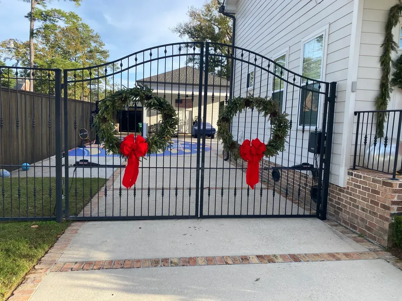 Black metal gate with wreaths and red bows, leading to a backyard with a pool.