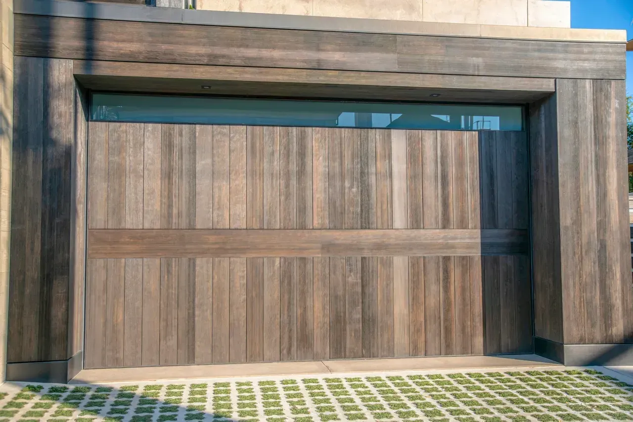 Wooden garage door with horizontal band and window, framed by wood paneling.