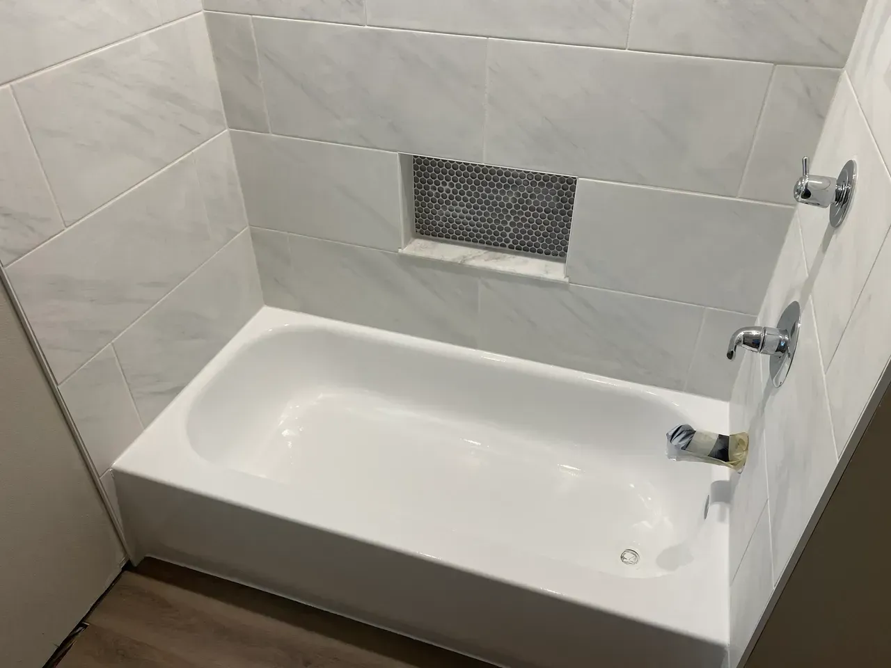 White bathtub with tiled walls and a small mosaic accent. Faucet and shower controls are visible.