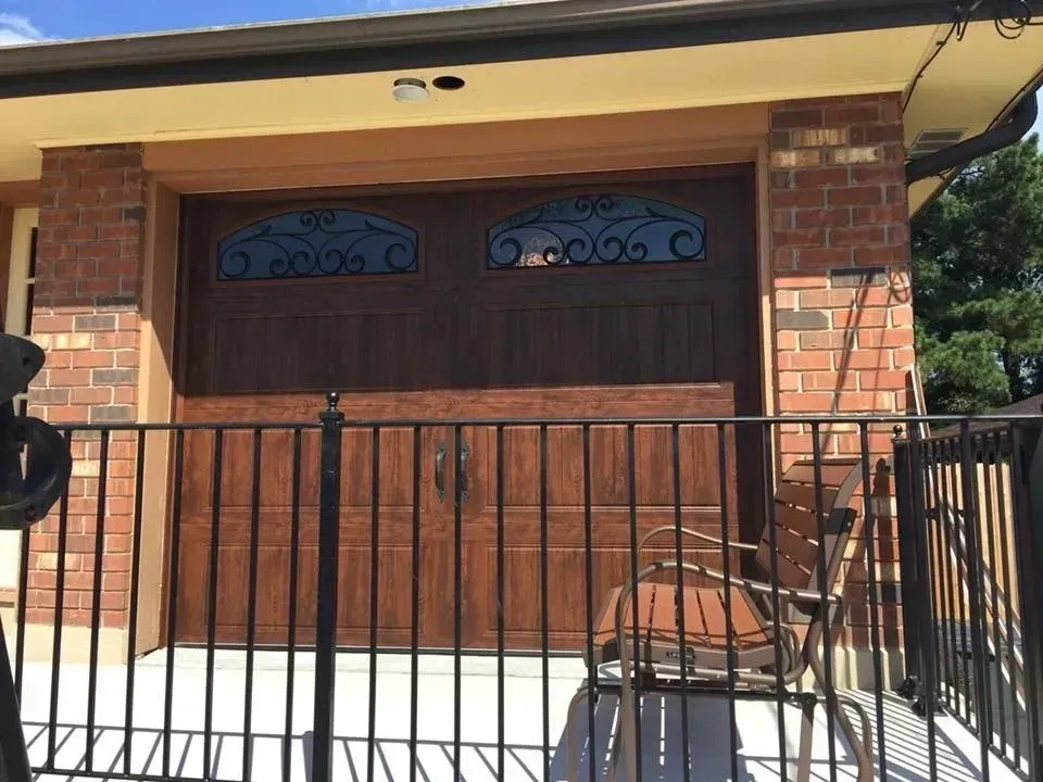 Brown garage door with decorative glass, brick facade, and black railing.