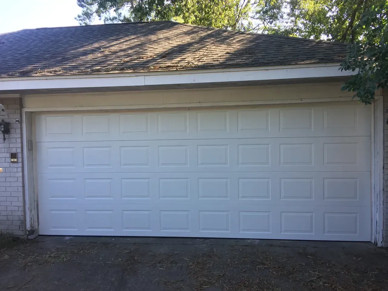 White garage door with grid pattern, set in a light-colored building, under a brown roof.