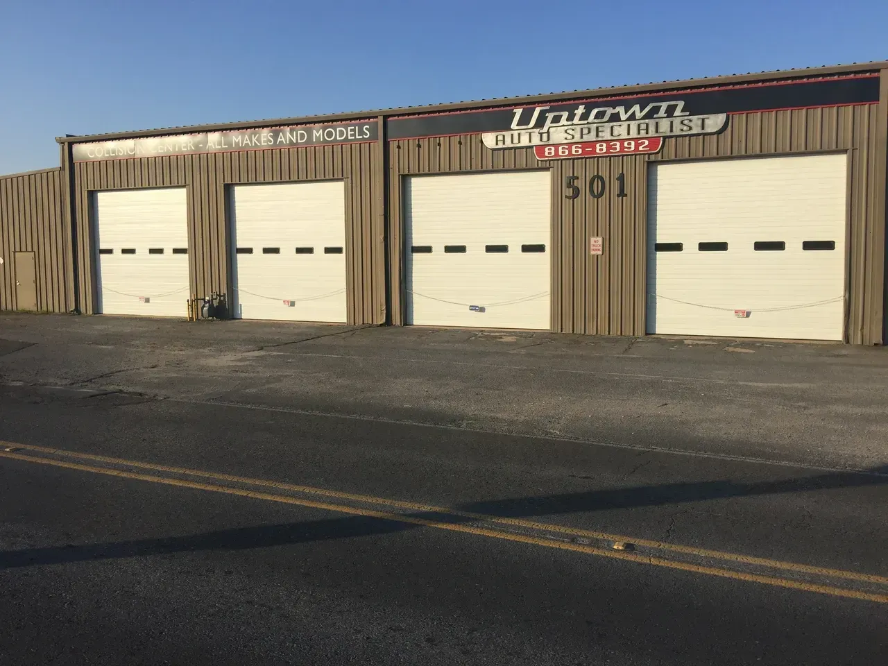 Uptown Auto Repair building with three garage doors. Black asphalt road. Sign says